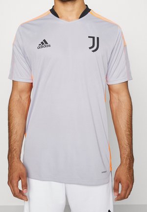 Jersey deportivo de manga corta en gris claro con cuello negro y logo de Adidas, con acentos naranja en los hombros y los lados.