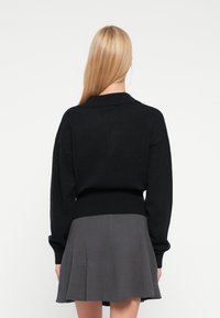 Pulover negru tricotat cu guler, mâneci lungi și tiv striat, asortat cu o fustă plisată gri.