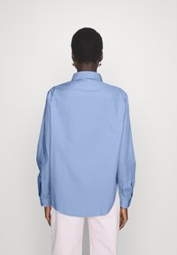Ljusblå bomullsskjorta med knäppkrage, långa ärmar och rundad nederkant. Har en slät yta och avslappnad passform.