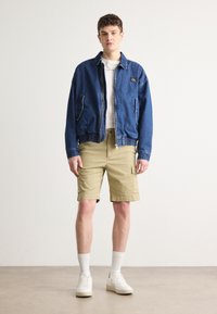 Denim jacket with a zip closure and elastic waist, paired with khaki cargo shorts. White t-shirt underneath and white sneakers.