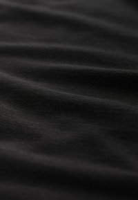 Tissu noir à texture douce, présentant de légères ondulations et plis, mettant en valeur la finition lisse et mate du matériau.