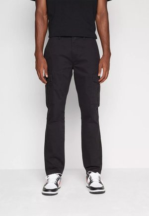 Pantalones cargo negros con bolsillos laterales, corte recto y tejido duradero. Combinados con zapatillas negras y blancas con detalles en rojo.