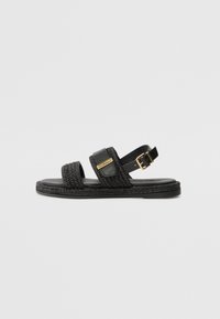 Sorte vævede sandaler med to stropdesign, der har en glat læderdetalje og guldfarvet hardware. Flad sål med tekstureret kant.