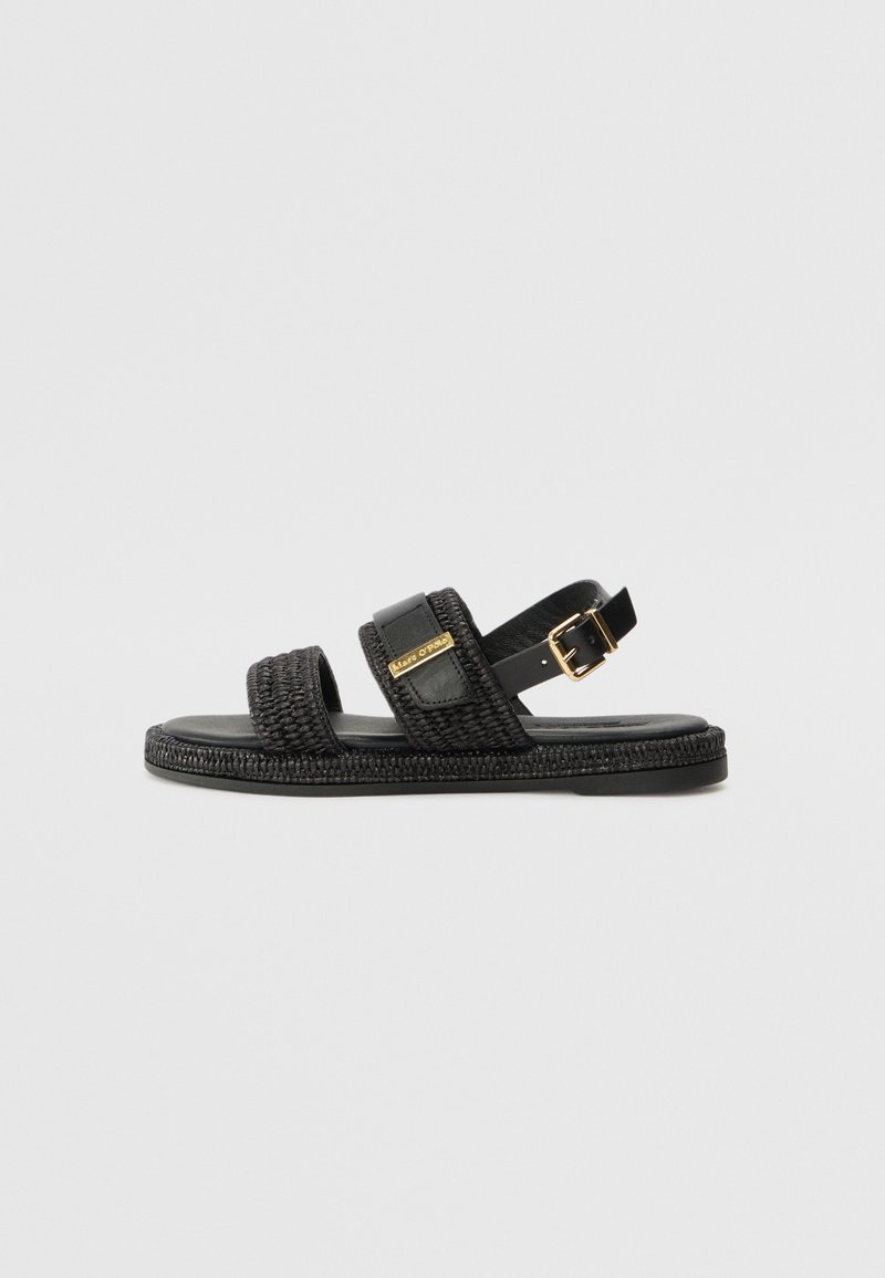 Sorte vævede sandaler med to stropdesign, der har en glat læderdetalje og guldfarvet hardware. Flad sål med tekstureret kant.