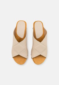 Sandales en cuir beige à enfiler avec un design entrecroisé, orteils découverts et semelle en bois. Présentent une texture lisse et une légère cambrure pour le confort.