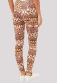 Leggings estampados que presentan tonos terrosos de marrón, rojo y crema con diseños geométricos. Llevados con zapatillas blancas.
