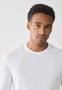 Weißes Langarm-T-Shirt mit rundem Ausschnitt, aus weichem Baumwollmaterial, das ein minimalistisches Design und eine glatte Textur aufweist.