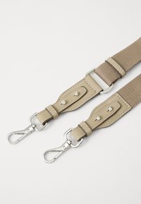 Beige adjustable strap with a fabric section and leather ends, featuring silver hardware and decorative studs on a smooth surface.