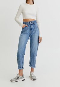 Jeans de tiro alto en azul claro con puños enrollados, con un corte holgado y cinco bolsillos, combinados con un top corto de manga larga de canalé blanco.