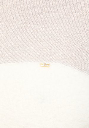 Tessuto lavorato a maglia color crema e beige con un piccolo ornamento rettangolare in oro e strass posizionato al centro vicino alla cucitura.