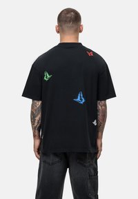 T-shirt nera in cotone con design di farfalle multicolori (verde, rosso, blu, bianco) su tutta la schiena, maniche corte e vestibilità comoda.