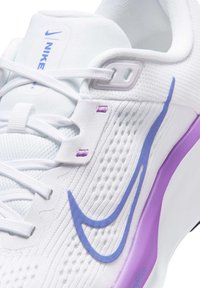 Chaussure de sport blanche avec une tige en mesh respirant agrémentée d'accents lavande, un design incurvé et lisse, et un col rembourré pour le confort.