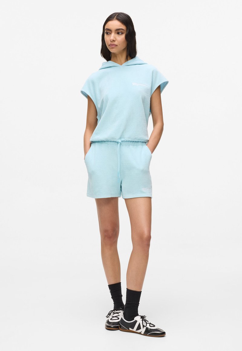 Ensemble sweat à capuche et short bleu clair en tissu doux. Le short est équipé d’un cordon de serrage, et le design est simple sans motifs.