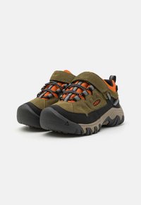 Wanderschuhe verfügen über ein olivgrünes Obermaterial, orangefarbene Akzente, eine schwarze Gummikappe und strukturierte Sohlen mit einem robusten Profildesign.