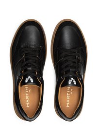 Zapatillas de cuero negras con suela de goma marrón, que presentan detalles perforados, cordones negros y un logo dorado en la plantilla.