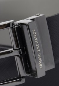 Zwarte riem met een gestructureerd oppervlak en een gepolijste zilverkleurige metalen gesp, gegraveerd met "Armani Exchange."