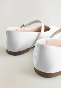 Bailarinas de satén blanco con una suela baja marrón, que presentan una correa con una hebilla plateada y una textura suave y lisa.