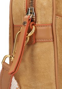 Tan suède handtas met een gladde leren strap, gouden hardware en een ritssluiting. Bevat contrasterende stiksels en een decoratieve accent.