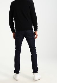 Mörkblå denimjeans med slim fit, med en standard femficksdesign och en mörk skjorta som bärs med vita sneakers.