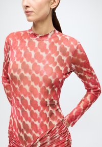 Haut à manches longues avec un motif abstrait rose et crème, fabriqué en tissu transparent avec des détails froncés à la taille.