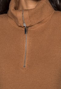 Pull marron côtelé à col montant avec fermeture éclair à moitié, garniture métallique, tissu texturé et coupe ajustée.