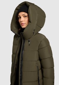Olivovo zelená prešívaná bunda s veľkou kapucňou, zipsom a bočnými vreckami. Hladký povrch s prešívaným vzorom a čiernymi akcentmi.