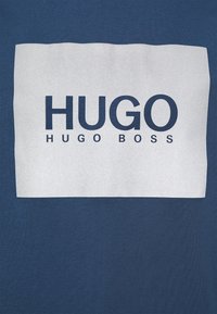 Niebieska bawełniana koszulka z białą prostokątną grafiką i wyraźnym czarnym napisem "HUGO HUGO BOSS". Gładka struktura z luźnym krojem.