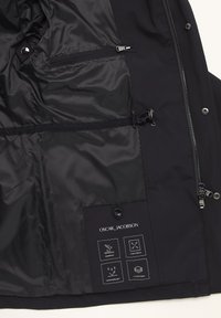 Sort vandtæt jakke med en glat stofoverflade, der har lynlås- og trykknaplommer samt en mærket inderside, der viser funktionsikoner.