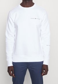 Sweatshirt blanc à col rond, logo "TOMMY HILFIGER" brodé en rouge et gris, poignets et ourlet côtelés, tissu doux en mélange de coton.