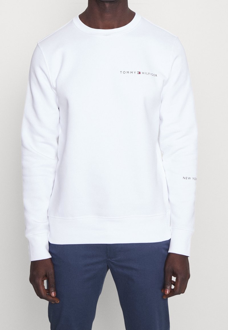 Sweatshirt blanc à col rond, logo "TOMMY HILFIGER" brodé en rouge et gris, poignets et ourlet côtelés, tissu doux en mélange de coton.