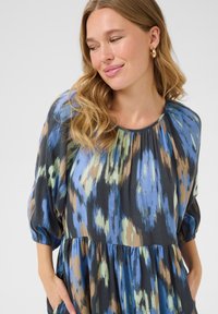 Vestido multicolorido con escote redondo, mangas abullonadas y cintura fruncida. La tela presenta una mezcla de patrones en azul, verde y marrón.
