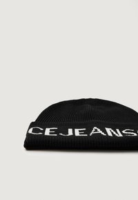 Gorro de malha preto com textura canelada e letras brancas que dizem "CEJEANS." O design apresenta uma dobra na base.