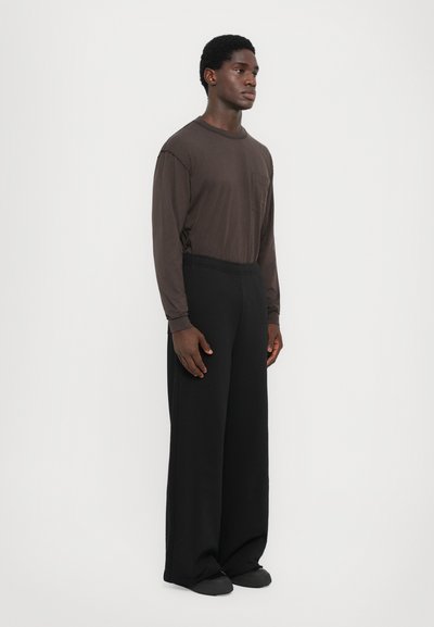 Brown long-sleeve shirt with a pocket, paired with loose black trousers. The fabric appears smooth, with a relaxed fit and uniform color.