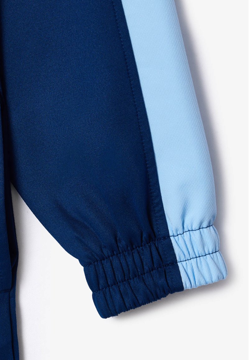 Pantalones deportivos azul marino con una franja lateral azul claro, que cuentan con puños elásticos y una tela suave y texturizada. Diseño limpio con colores bicolor.