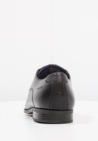 Zapato de cuero negro con un acabado suave y tacón texturizado. Detalles de costura visibles a lo largo del costado y suela de goma plana.