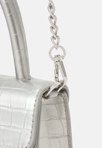 Srebrna syntetyczna torebka z teksturowanym wzorem krokodyla, wyposażona w górną rączkę i łańcuszkowy pasek.