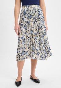 Plissierter Midirock in Creme mit blauem und schwarzem Blumenmuster, elastischem Bund und weichem, leichtem Stoff. Kombiniert mit schwarzen Slingback-Schuhen.