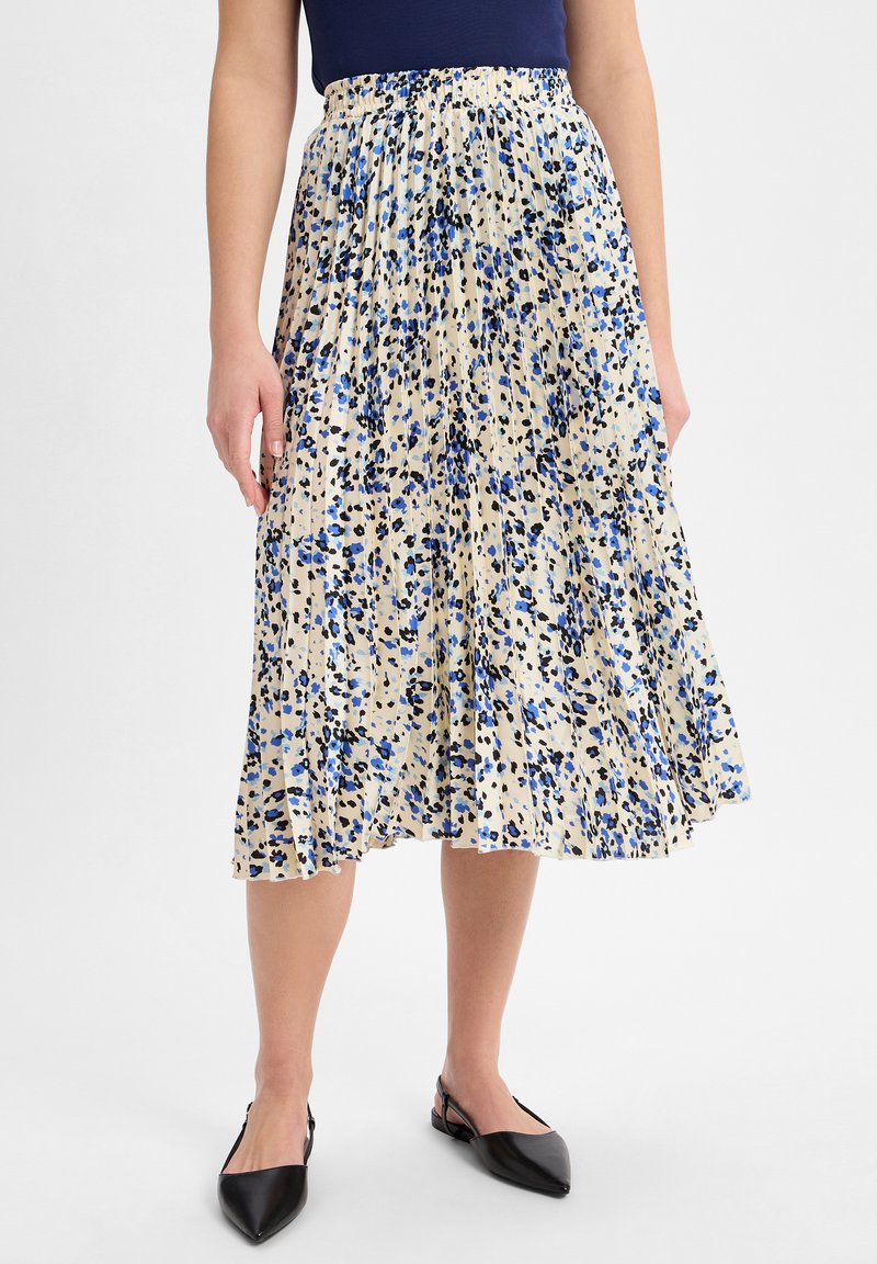 Plissierter Midirock in Creme mit blauem und schwarzem Blumenmuster, elastischem Bund und weichem, leichtem Stoff. Kombiniert mit schwarzen Slingback-Schuhen.