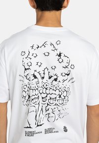 Hvid bomuld t-shirt med et stort sort grafisk motiv af et træ med tegneserieagtige ansigtstræk, tekst i bunden, og et afslappet fit design.