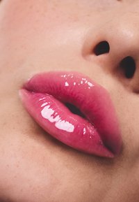 Labios rosados brillantes con una textura suave, que reflejan la luz, sobre un fondo de piel suave con ligeras pecas.