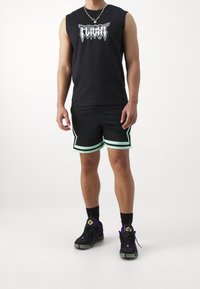 Czarna koszulka bez rękawów z nadrukiem "FLIGHT", czarne szorty z miętowym wykończeniem oraz fioletowo-czarne sneakersy z czarnymi sznurówkami.