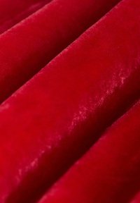 Nahaufnahme eines roten Samtstoffs, der eine weiche, glatte Textur zeigt, mit Falten, die Schatten und Highlights erzeugen.