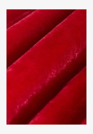 Detailní záběr červeného sametu ukazující jemnou, hladkou texturu s vlnami vytvářejícími stíny a odlesky.