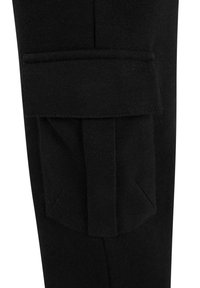 Pantalones de tela negra en primer plano que muestran un bolsillo cargo rectangular con una gran solapa asegurada en la parte superior.