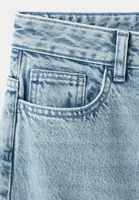 Jean en denim bleu clair en gros plan montrant la poche avant, la petite poche à monnaie, la passants de ceinture et les coutures détaillées sur le tissu.