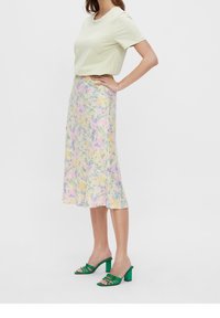 Lichtgroene T-shirt met korte mouwen, gecombineerd met een bloemen midi-rok in pastelkleuren. Groene haksandalen vullen de outfit af.