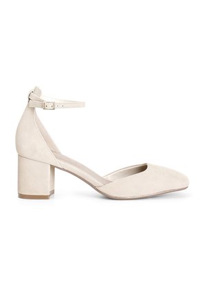 Scarpa beige in suede con tacco a blocco, punta affilata e cinturino alla caviglia. Superficie testurizzata con interno liscio e design minimalista.