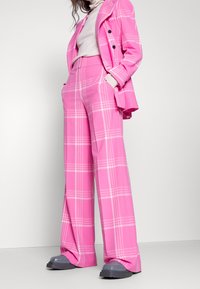 Costume écossais rose vif avec veste croisée et pantalon à jambes larges. Conçu avec des lignes blanches contrastantes. Le matériau semble lisse.
