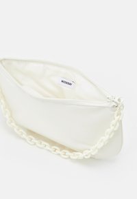 Pochette blanche à texture lisse, dotée d'une fermeture éclair et d'une bandoulière chaîne décorative. L'intérieur est doublé d'un tissu étiqueté.