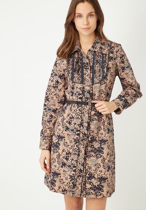 Vestido camisero de tejido suave y estampado. Presenta un fondo beige con diseños florales azules, botones en la parte delantera y cinturón en la cintura.